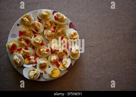 Plate Of Deviled Eggs Garnished With Red Pepper On Linen Tablecloth. Stock Photo