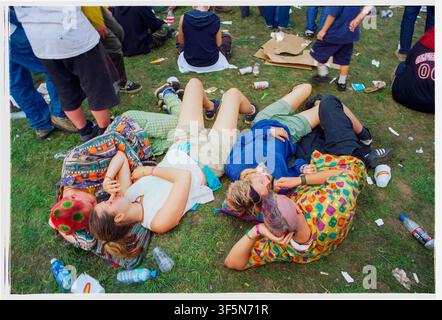 COLORFUL FRIENDS CHILLING ON THE FESTIVAL GRASS READING FESTIVAL 1999, ROCK FANS AND CROWD SCENES, READING, ENGLAND, 1999: Four young people in colourful and patterned clothing, including one with dyed red hair, relax together on the grass surrounded by empty plastic bottles. Photo: Rob Watkins. INFO: During the late 1990s, the Reading Festival became Britain's premier alternative music event, featuring rock, indie, punk, metal, electronic and emerging artists. Its diverse line-up attracted huge crowds and helped define the era's vibrant festival culture. Stock Photo