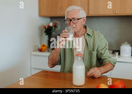 Smiling senior man drinking milk in kitchen. Stock Photo