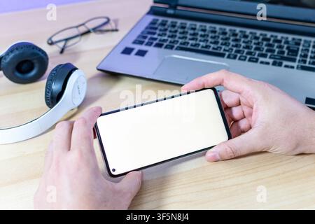 A person holds a smartphone in landscape mode, ready for gaming or watching a movie. Blank screen for mockup purposes. Stock Photo
