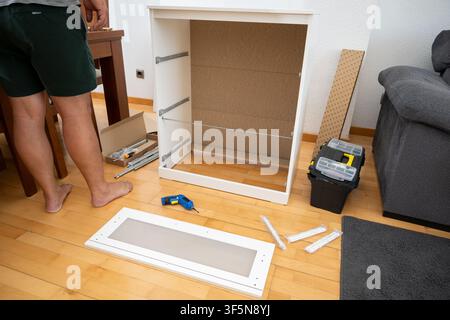 Man is assembling new furniture, using tools on a wooden floor at home Stock Photo