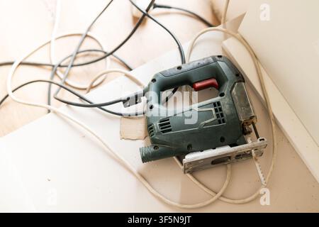 Using a jigsaw tool to cut wood materials at a home improvement workspace. Tangled electrical cords and wood shavings are visible on the work surface.  Stock Photo