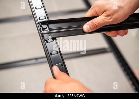 Engaging in assembly of metal frame sections using precision connectors at a workspace. Well-organized setting with tiled flooring and other parts visible in the background.  Stock Photo
