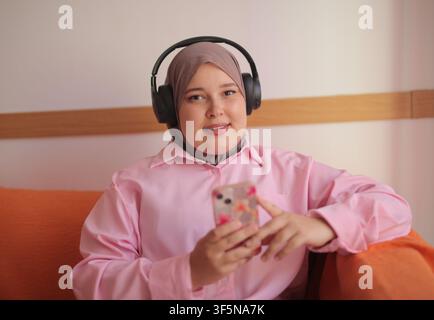 Happy woman in hijab listening to music on headphones Stock Photo