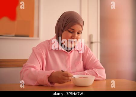 Smiling woman wearing a hijab eats her breakfast Stock Photo