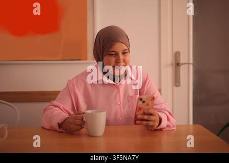 Young woman in hijab enjoys coffee on her phone Stock Photo