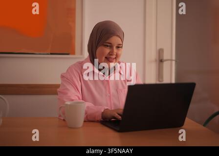 Smiling Muslim woman working on a laptop at home Stock Photo