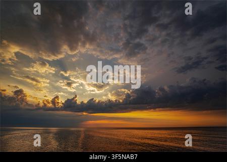 Sunbeams breaking through storm clouds over calm ocean at sunset Stock Photo