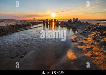 Small stream flowing into sea on beach at sunset Stock Photo