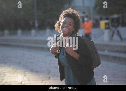 Joyful young woman with backpack smiles in city Stock Photo