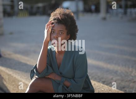 Thoughtful young woman sitting outside in sunlight Stock Photo