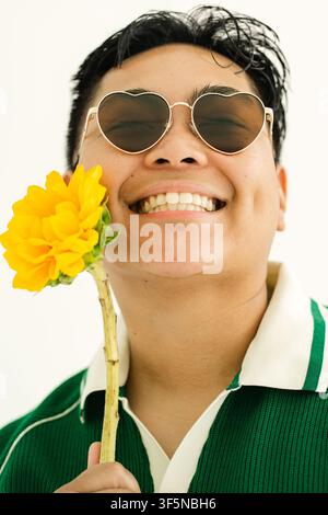 Cheerful person wearing heart sunglasses holds a sunflower Stock Photo