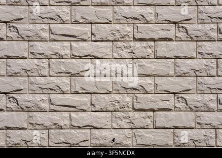 Light gray stone wall with decorative rectangular bricks and deep relief textures. Modern cladding material with rough split surfaces for a clean arch Stock Photo
