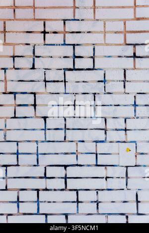 White brick wall with blue spray paint leaks and dark vertical seams. Weathered brickwork surface with concrete mortar lines and small yellow detail f Stock Photo