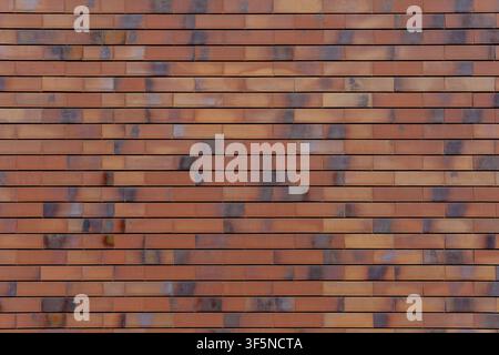 Modern clinker brick wall with smooth rectangular bricks and dark thin seams. Variegated terracotta surface with brown and black burn marks for a cont Stock Photo