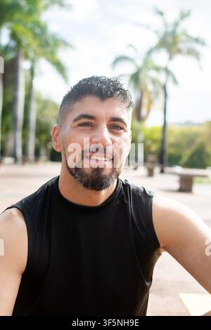 Portrait of a smiling athletic man taking a break after exercising outdoors in a tropical park. Stock Photo