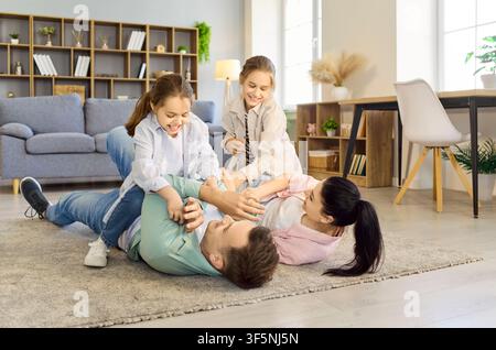 Happy family tickling play on living room floor, parents and daughters laughing Stock Photo