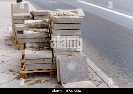 Pavement tiles stacked on wooden pallets along an urban road. Concrete paving blocks for sidewalk reconstruction and city renovation works. Stock Photo