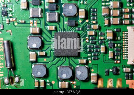 Detailed macro shot of a green printed circuit board (PCB) featuring a central integrated circuit microchip surrounded by surface-mount technology Stock Photo