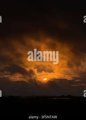 Dramatic orange sunset glowing through dark clouds over the horizon Stock Photo