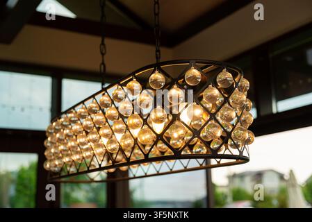 A close-up view of a contemporary chandelier hanging from the ceiling, featuring a rectangular metal frame adorned with rows of clear glass orbs. The Stock Photo