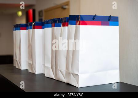 Several neatly arranged white gift bags with blue and red designs near the top are displayed on a dark countertop, ready to be distributed at an event Stock Photo