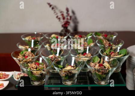 An array of individual salad servings is elegantly presented in glass cups on a buffet table. Each cup contains a mixture of greens, shredded meat, ch Stock Photo