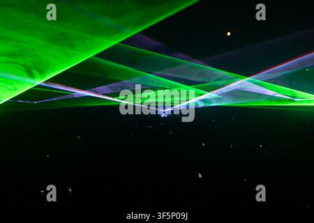 Spectators gather in excitement as vibrant green and blue laser beams illuminate the night sky at an outdoor concert. The atmosphere buzzes with energ Stock Photo