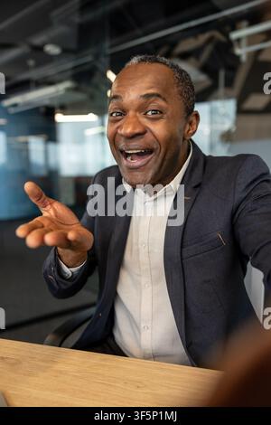 Confident mature businessman with expressive gesture engaging in an enthusiastic discussion during a virtual meeting. Communicating success and positive collaboration from his modern office workplace Stock Photo