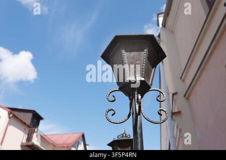 Blue sky background vintage street lantern photo. Retro outdoor lamp post with forged iron scrolls stands against sunny clouds. Antique classical city Stock Photo