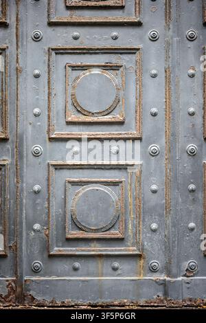 An old rusty metallic door featuring geometric decorative shapes, studs, and weathered iron surface texture. Stock Photo