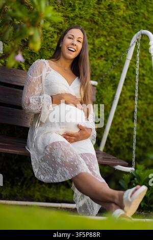 Expectant mother smiling warmly while sitting outdoors on a garden swing Stock Photo