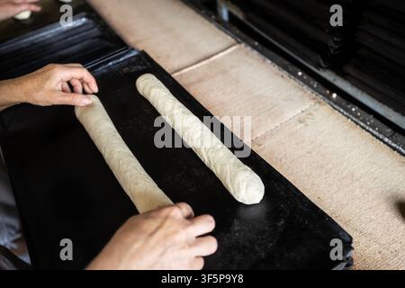 Baker preparing dough on a tray in a commercial kitchen facility where raw bread rolls are carefully shaped by skilled hands for the oven in a traditi Stock Photo