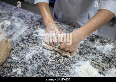 Professional baker hands kneading fresh dough on a granite countertop in a rustic commercial kitchen environment for artisan bread making process in a Stock Photo