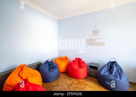 Colorful bean bag chairs arranged on wooden parquet flooring in a bright cozy corner of a modern room with light blue walls and a minimalist cup and b Stock Photo