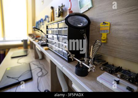 Electronic repair workshop a soldering station with a magnifying glass tool, plastic storage drawers for small parts, circuit boards, and various hand Stock Photo