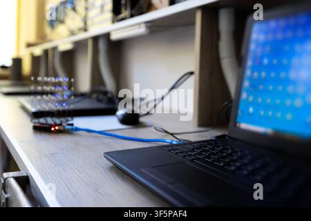 Electronic components connected to laptop on desk and light emitting diodes glowing blue lights for engineering testing in a laboratory space computer Stock Photo