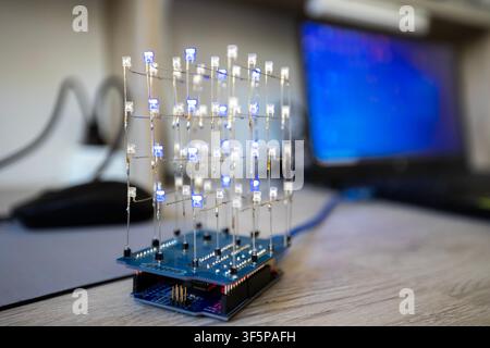 Led light cube on a desk with blurred computer display in the background electronic circuit board project components on wooden surface with wires and Stock Photo