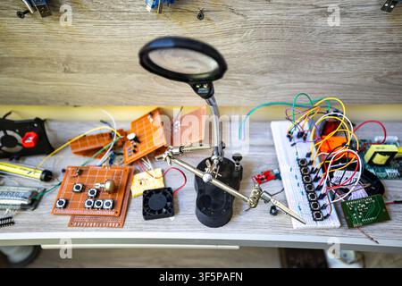 Electronic components and tools on a cluttered workbench for technical hobby projects a magnifying lamp with helping hands, scattered circuit boards, Stock Photo