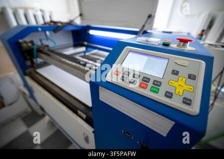 Cnc laser cutting machine for precision manufacturing with blue metal frame, digital control interface, operational keypad, emergency stop button, and Stock Photo