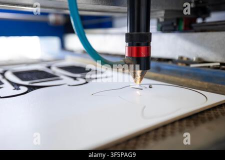 Industrial cnc laser cutting machine engraving a creative white plastic sheet with a precision nozzle in a workshop setting, surrounded by mechanical Stock Photo