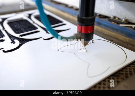 Laser cutting machine engraving custom patterns on white material with precision beam nozzle inside industrial workshop, bright focused glow marks sur Stock Photo