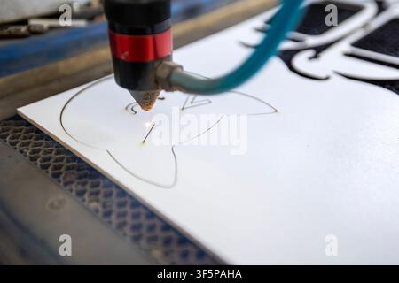 Industrial cnc laser cutting machine shaping white plastic material with precision beam during manufacturing process in workshop area surrounded by sp Stock Photo