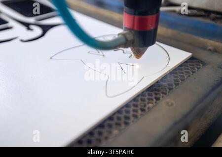 Professional cnc laser cutting machine crafting a white material with cat design shapes in a industrial workshop setting a honeycomb base plate and bl Stock Photo