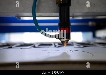 Industrial cnc laser cutting machine engraving intricate designs on white material with precision optics and blue tubing in a professional workshop en Stock Photo