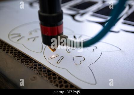 Cnc laser cutting machine engraving a cat pattern on a white plastic sheet with a precision nozzle and intense beam in a workshop setting using automa Stock Photo