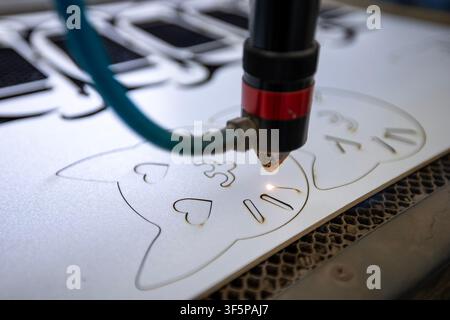 Laser cutter machine engraving cat designs on a white plastic sheet with a precision beam inside a workshop industrial space metal grid supports and b Stock Photo