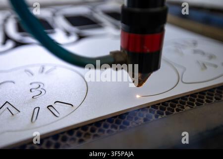 CNC laser cutting machine creates precise patterns on a flat white material sheet using a focused beam, automated industrial technology process, metal Stock Photo