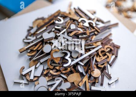 A pile of assorted laser cut wooden shapes including letters and abstract symbols rests on a flat surface scattered in a workshop area with bits of le Stock Photo