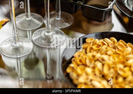 Elegant glass stemware arranged on a reflective table surface next to a dark bowl containing empty pistachio shells, on the crystal bases and soft hig Stock Photo